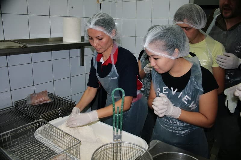 Процесс панировки После того, как мы обмундировались и продезинфицировались, нас все же впустили в обитель курицы. Находиться внутри ресторана было крайне неуютно, вследствие того, что мы были голодные. Запахи, которые тешили наши рецепторы еще и будоражили воображение. Первое что нам удалось увидеть – это панировочный стол. Мне было очень интересно увидеть, как же получается такая гранулированная фактура на крылышках.
